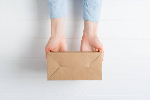 Rectangular cardboard box in female hands. Top view, white background - Photo, Image