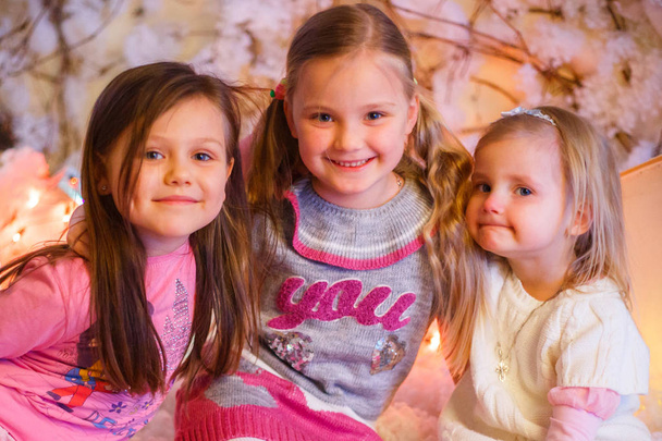 drie meisjes knuffelen en glimlachen in het nieuwe jaar decoraties met kunstsneeuw en kleine kartonnen huizen - Foto, afbeelding