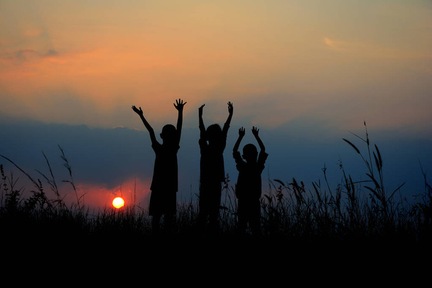 Чорний силует трьох дітей, що стоять разом. На заході сонця є небо
. - Фото, зображення