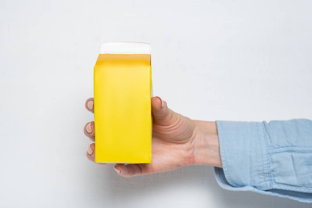 Yellow carton box or packaging of tetra pack in a female hand. White background - Fotó, kép