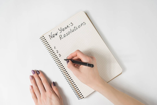 Phrase New Year's resolutions in the notebook. Female hands with pen - Photo, Image