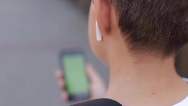 Mock up of teenage boy with wireless headphones use phone otside. Green screen - Footage, Video