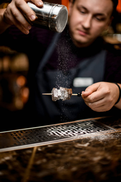 Professional bartender adding a sugar powder to the brownie pieces on the skewer - Zdjęcie, obraz