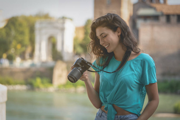 Улыбающаяся девушка в итальянском городе, смотрящая на экран камеры
.  - Фото, изображение