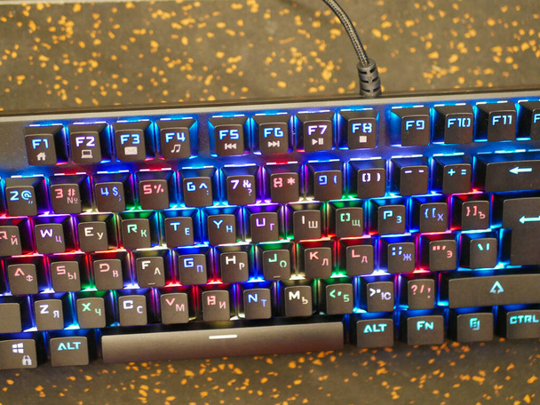 RGB toetsenbord. Een kleurrijk toetsenbord schittert met verschillende kleuren. liggend op tafel. Zachte bokeh - Foto, afbeelding