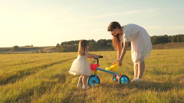 Mama uczy córkę jeździć na rowerze. Matka gra z jej małą córką. małe dziecko uczy się jeździć na rowerze. koncepcja szczęśliwego dzieciństwa. - Zdjęcie, obraz