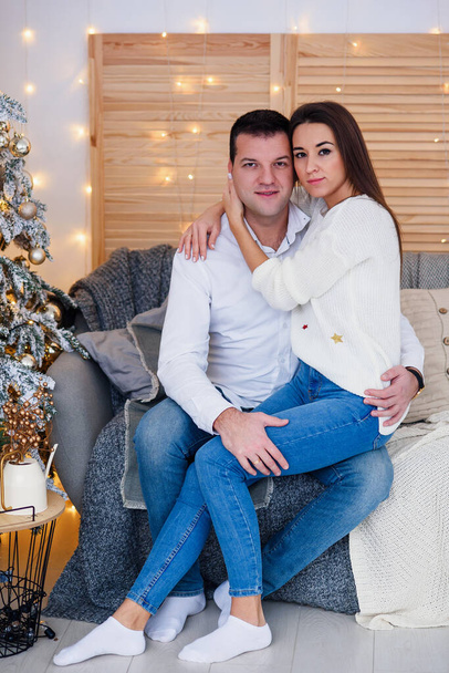 Attractive cheerful man and woman sitting near christmas tree and hugging each other. New Years eve. - Foto, Bild