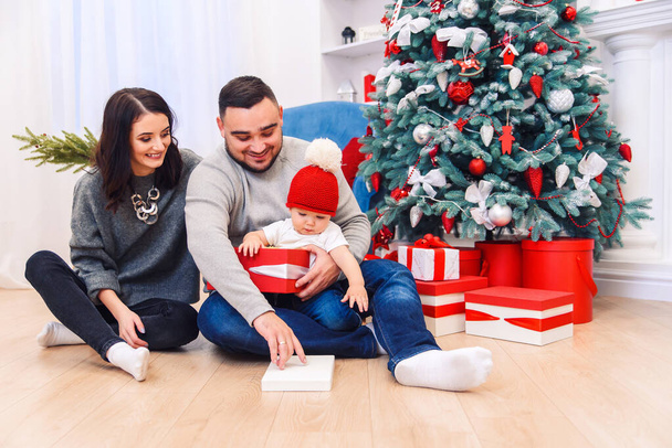 Young parents help to unpacking the first Christmas gift to their newborn child. Toddler boy receives his first christmas gift. - Foto, Imagem