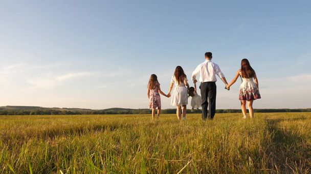 太陽の下で姉妹が畑を歩いている母と父と娘幸せな若い家族だ子供たち、お父さんとお母さんは太陽の下で牧草地で遊ぶ。幸せな家族という概念は. - 写真・画像