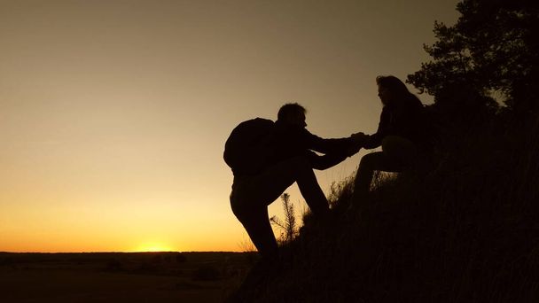 žena cestovatel drží ruku muže cestovatele pomáhá vylézt na vrchol kopce. Turisté šplhají na horu při západu slunce a drží se za ruce. týmová práce obchodních partnerů. Šťastná rodina na dovolené. - Fotografie, Obrázek