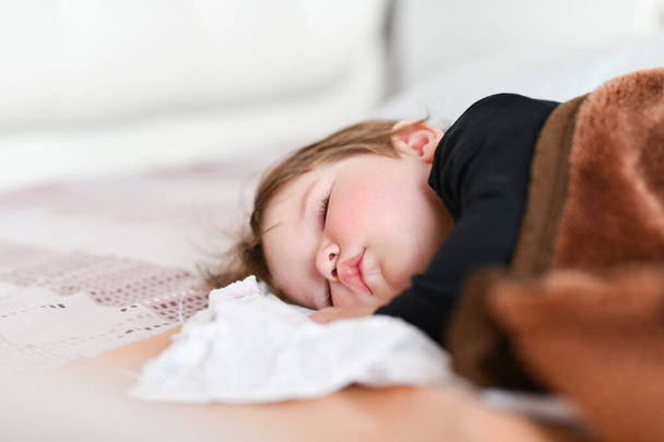 Babys tagsüber schlafen. gesunder Tagesschlaf für das Neugeborene. Das Kind schläft in einem orthopädischen Kinderkokon auf dem Bett. Kinderpause nach aktivem Spielen mit den Eltern - Foto, Bild