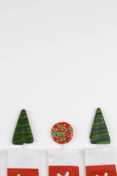 Κόκκινα και πράσινα γλειφιτζούρια με κόκκινες κάλτσες σε λευκό φόντο. Πρόσκληση, Χριστουγεννιάτικη γιορτή - Φωτογραφία, εικόνα