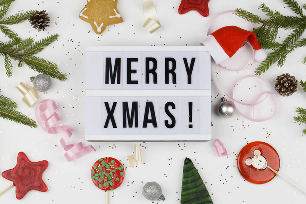 Веселые рождественские слова на светлой коробке с красными и зелеными леденцами, ветви елки, лента и украшения на белом фоне
 - Фото, изображение