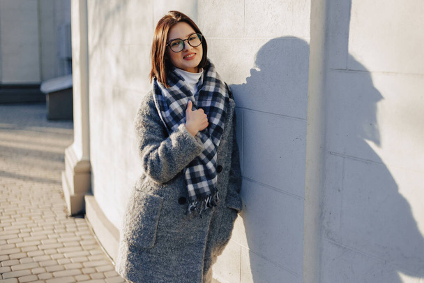 Attractive young girl wearing glasses in a coat walking on a sunny day - Photo, image