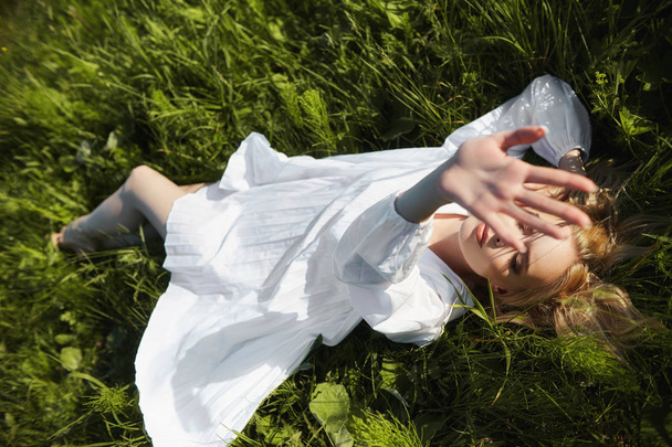 Girl in a long white dress lies on the grass in a field. Blonde  - Fotografie, Obrázek