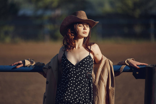 Lány cowboy kalapban pihen a faluban, közel az istállókhoz, po - Fotó, kép