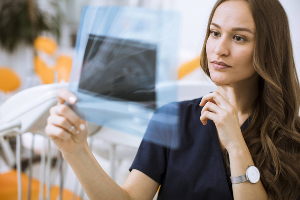 Красивая молодая женщина-врач в защитных перчатках осматривает рентген в кабинете дантиста
 - Фото, изображение