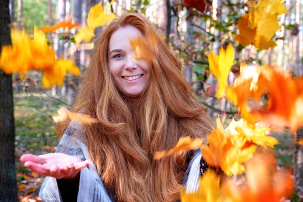 Kobieta z czerwonymi włosami, rzucanie liści klonu jesienią. - Zdjęcie, obraz