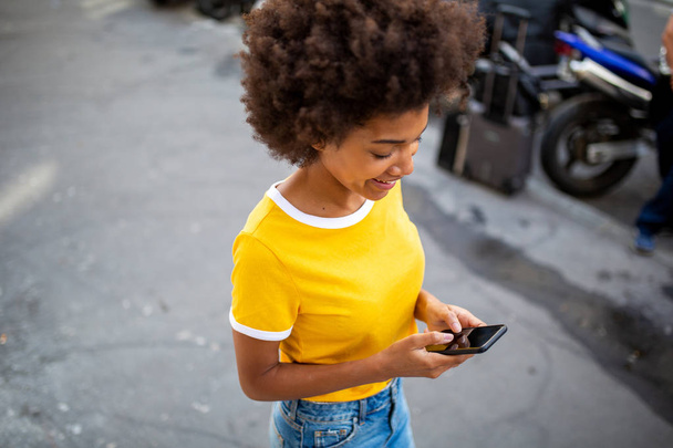 Portrait de jeune femme afro-américaine regardant un téléphone portable à l'extérieur dans la rue
 - Photo, image