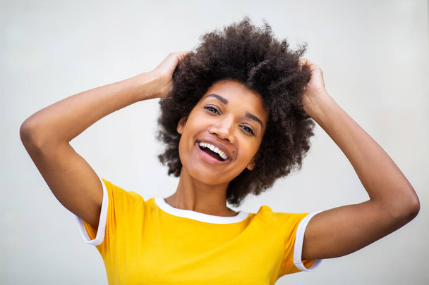 Nahaufnahme Porträt der schönen jungen schwarzen Frau mit lächelnden Händen im Haar vor weißem Hintergrund  - Foto, Bild