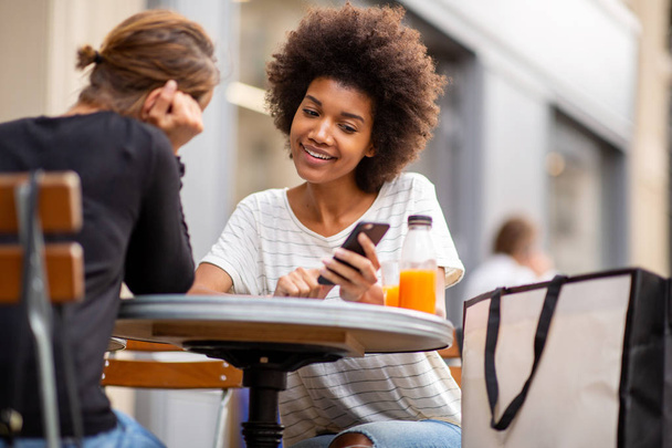 2人の若い女性が屋外カフェに一緒に座って携帯電話を見ている姿 - 写真・画像