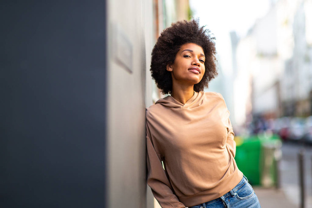 Portret piękny czarny kobieta moda model z afro fryzura opierając się o ścianę na zewnątrz - Zdjęcie, obraz