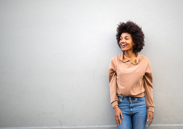 Portrait de heureuse jeune femme afro-américaine attrayante riant par un mur gris
 - Photo, image