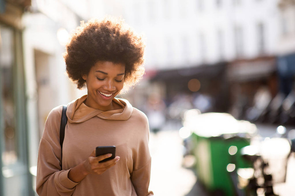 Portrait beautiful young black woman with phone walking in city - Foto, imagen