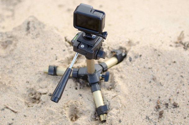 Екшн-камера стоїть на невеликому тринозі, записуючи відео на піщаному пляжі
. - Фото, зображення