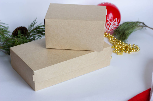 zwei Pappschachteln liegen übereinander auf weißem Grund inmitten der Weihnachtsdekoration, fichtengrüne Zweige - Foto, Bild
