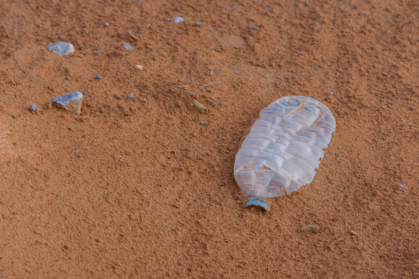 Plastic vervuiling en afval dumpen in de woestijn zand onder een boom. Bewustmaking van de noodzaak van milieubescherming, recycling en bescherming van de wereld. Milieuconcept. - Foto, afbeelding
