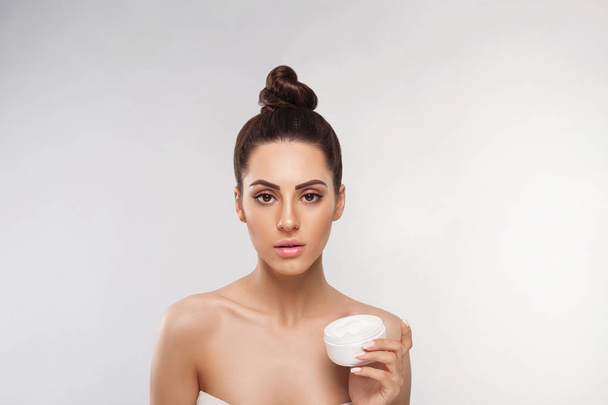 Skin care. Beauty Concept. Young woman holding cosmetic moisturizing cream. Soft skin and naked shoulders, model with light nude make-up, portrait of girl face with clean healthy skin. Dermatolog - Foto, imagen