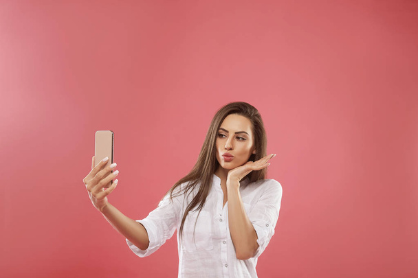 Portrait of a pretty girl taking a selfie isolated over pink background - Photo, Image