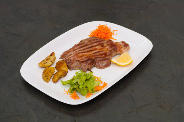 Juicy grilled meat steak with lemon, carrots, lettuce and potatoes. - Photo, Image