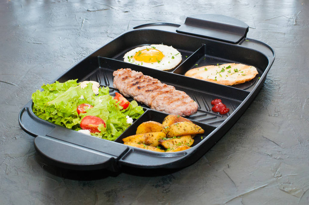 Breakfast, cutlet or steak, tomato salad, fried potatoes, croutons and fried egg on black plate. Restaurant serving lunch. - Fotó, kép