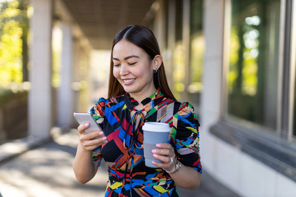 Atraktivní mladá žena s chytrým telefonem a kávou ve městě  - Fotografie, Obrázek