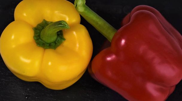 dvě jasně žluté a červené papriky na černé desce - Fotografie, Obrázek