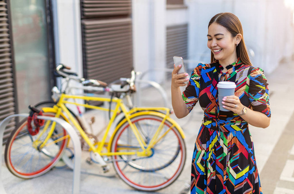 Young hipster woman with her bike and smartphone, drinking coffee - Photo, Image