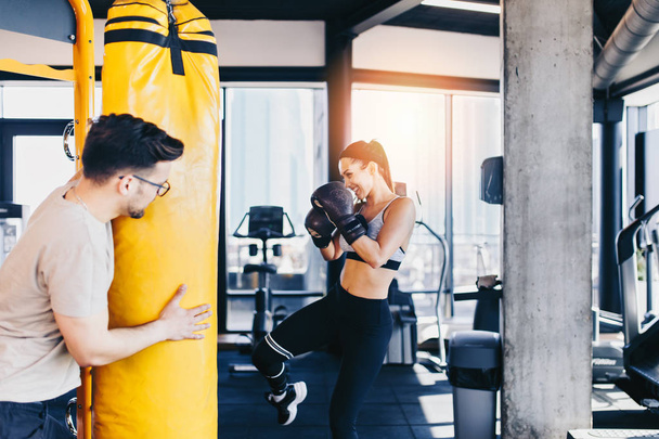 Young attractive woman with instructor on kickboxing training. She hitting or punching in big yellow boxing bag. - Photo, Image