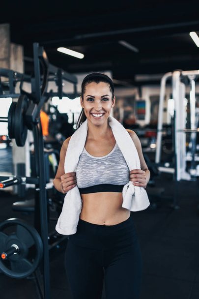 Young exhausted woman relaxing in fitness gym after successful workout wipes sweat from the forehead with white towel while holding water bottle in other arm. - 写真・画像