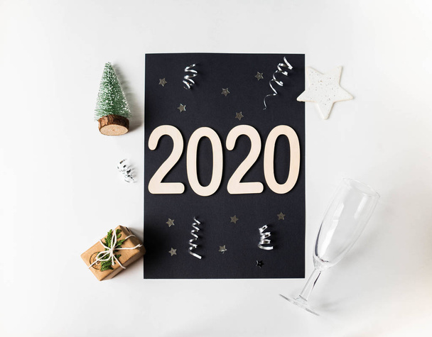 Flat lay white New year composition - Black card, white background, numbers 2020, Christmas tree, champagne glass, Christmas balls and gift. Top view - Photo, Image
