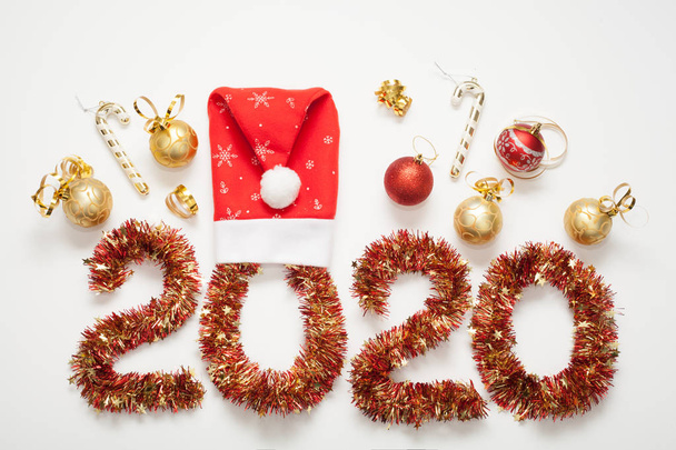 The figure 2020 is made of a red garland decorated with a Santa hat and gold toys and candies. isolated on white background. The concept of a New year. - Photo, Image