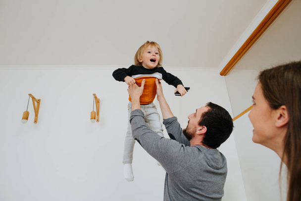 Happy young family moving to a new home, father throwing kid in the air. - Photo, Image
