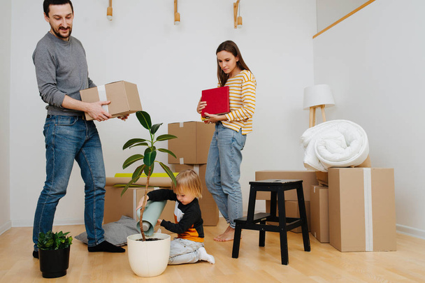 Family moved into a new apartment. Child watering plant while parents unpacking. - Fotografie, Obrázek
