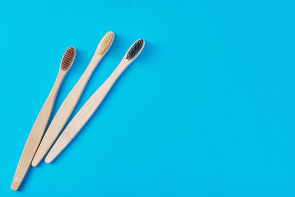 three wooden bamboo toothbrushes on a blue background, top view. - Photo, Image
