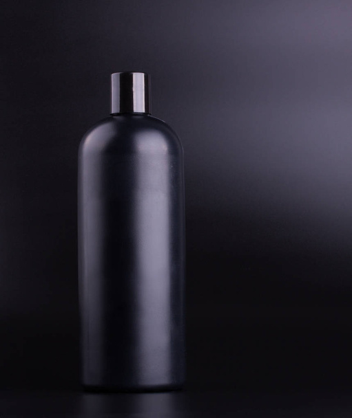 Чорна пляшка шампуню на чорному тлі
 - Фото, зображення