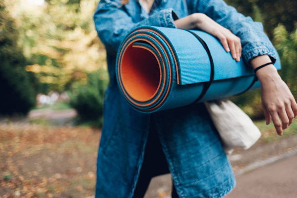 Girl with a sports mat in hands hurries to yoga class. Yoga mat closeup concept - Photo, Image