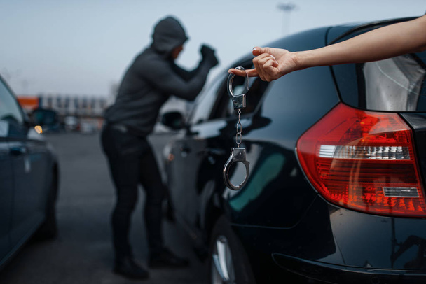 Car thief breaking door lock, criminal lifestyle, illegal work, burglar. Hooded male robber opening vehicle on parking, female hand with handcuff. Auto robbery, automobile crime, vandalism - Photo, image