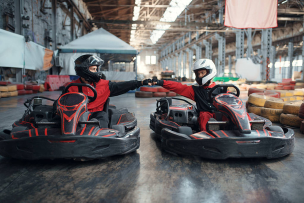 Two kart racers on start line, front view, karting auto sport indoor. Speed race on close go-cart track with tire barrier. Fast vehicle competition, high adrenaline leisure - Foto, afbeelding