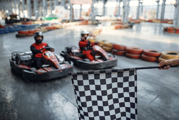 Two kart racers on start line, checkered flag, front view, karting auto sport indoor. Speed race on close go-cart track with tire barrier. Fast vehicle competition, high adrenaline leisure - Photo, Image